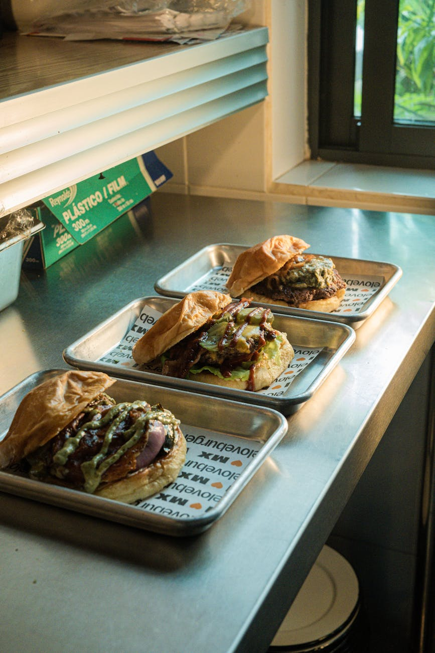 Counter-height view of a chain restaurant meal — a burger, a burrito bowl, and a half chicken plate side by side with a kilojoule menu board