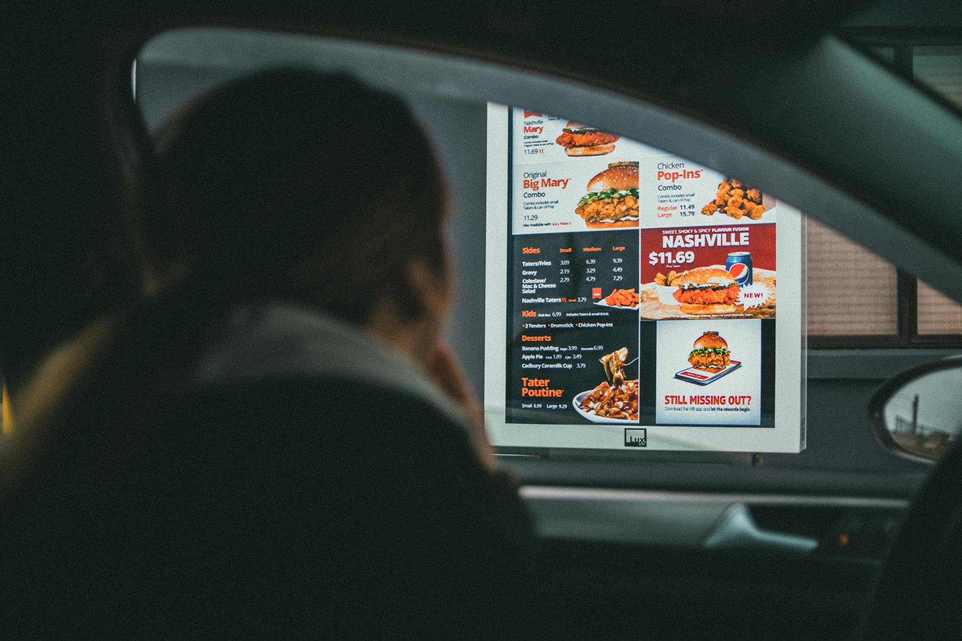 Australian chain restaurant meals on a counter — a half PERi-PERi chicken plate, a grilled chicken burrito bowl, a burger, and a bowl of pho with a kilojoule menu board behind