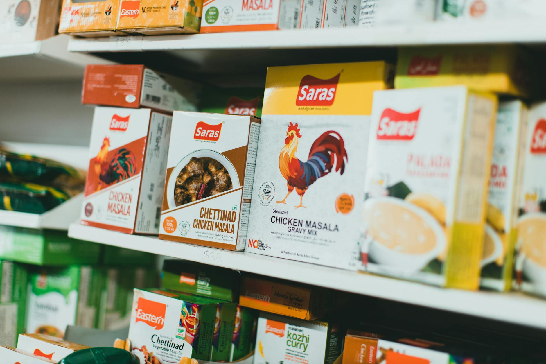 Open packaging of Coles and Woolworths chilled and frozen ready meals on a kitchen counter beside a small kitchen scale and a notepad showing kilojoule and protein numbers in a sunlit Australian kitchen