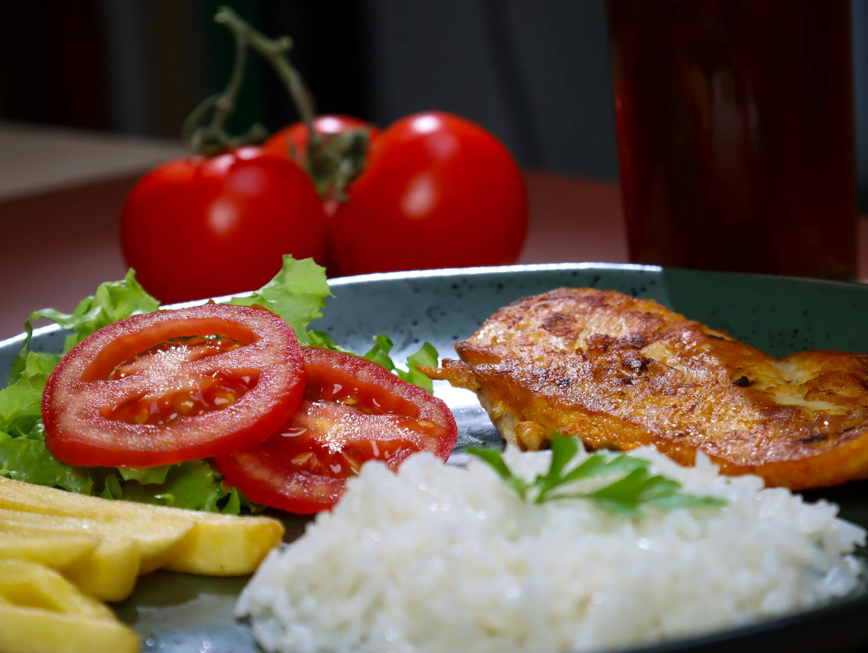 Colorful variety of foods including grilled chicken, rice, vegetables, fruit, and dark chocolate arranged on a kitchen counter
