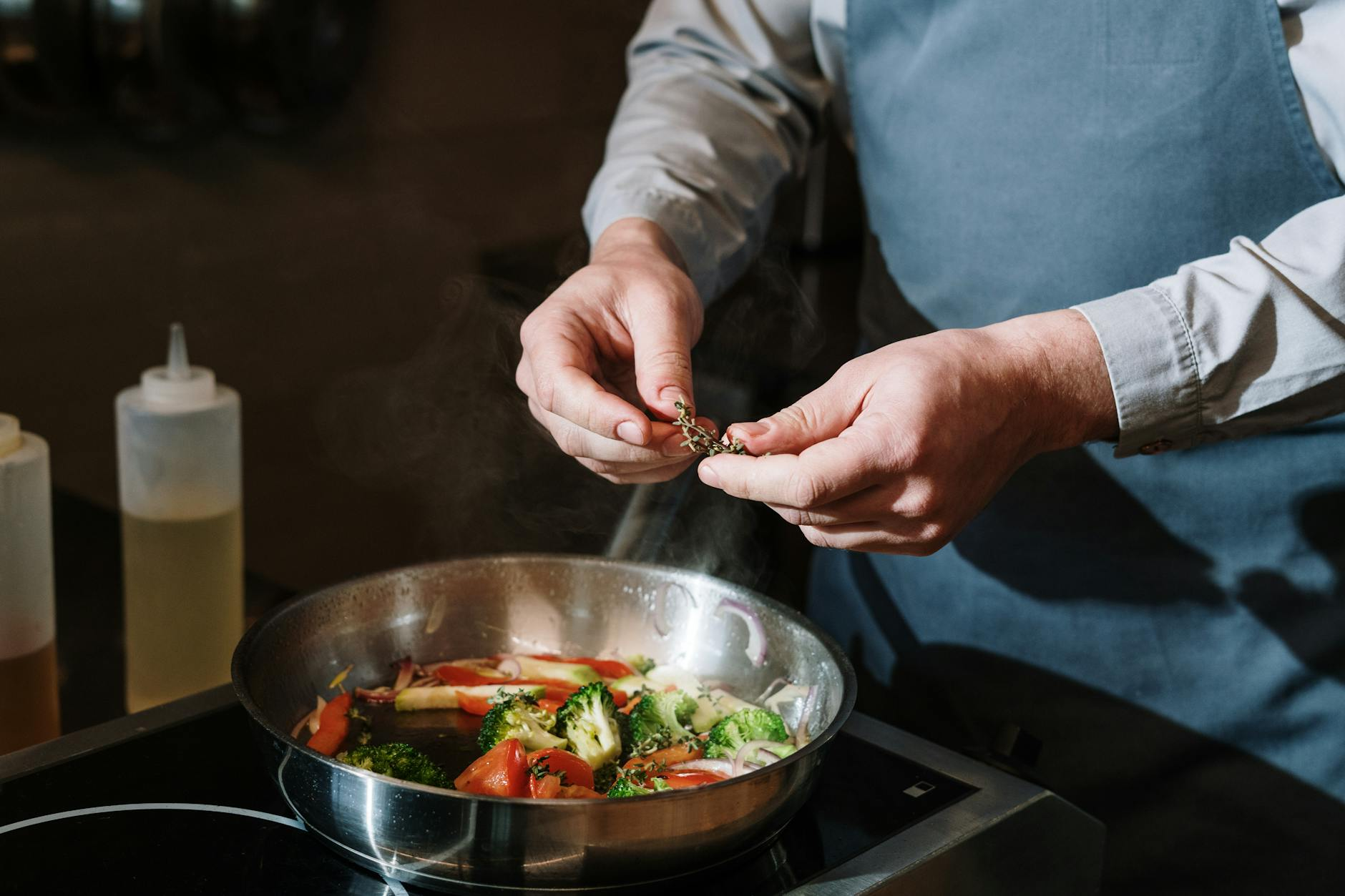 Person measuring olive oil with a tablespoon while cooking a healthy stir-fry with vegetables in a bright kitchen