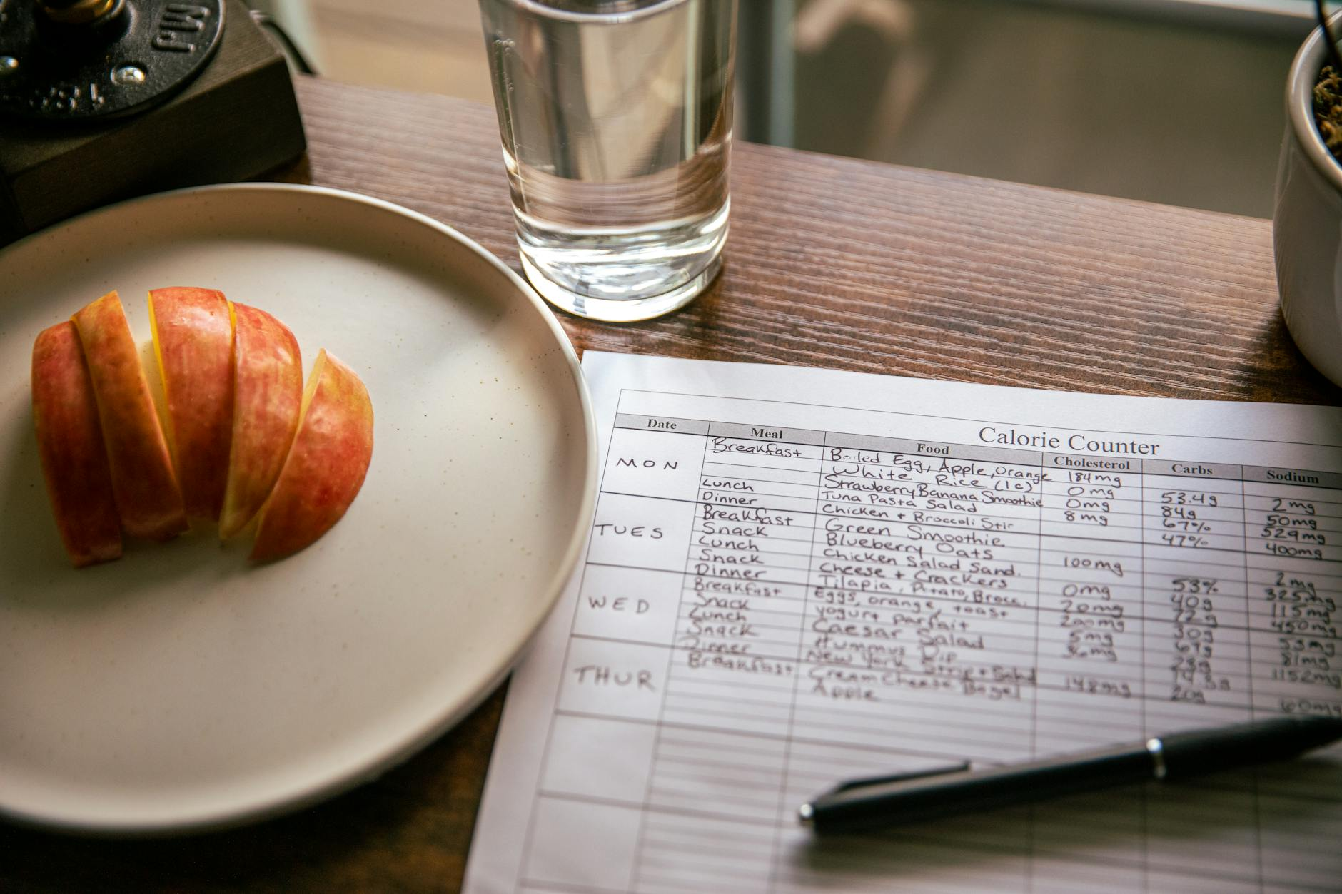 Smartphone displaying a calorie tracking app with weekly average kilojoule and protein totals beside a small kitchen scale weighing grilled salmon and a glass of water on an Australian kitchen counter