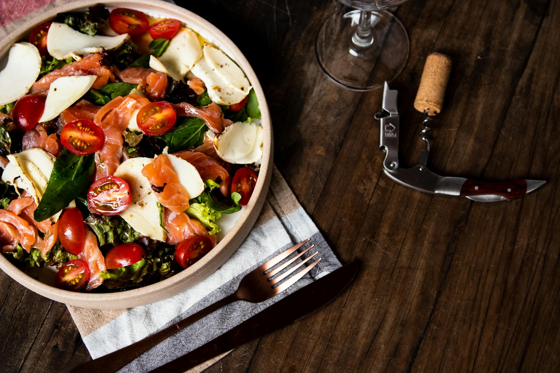 Person eating a colorful Mediterranean style meal with salmon, leafy greens, and olive oil at a sunlit kitchen table