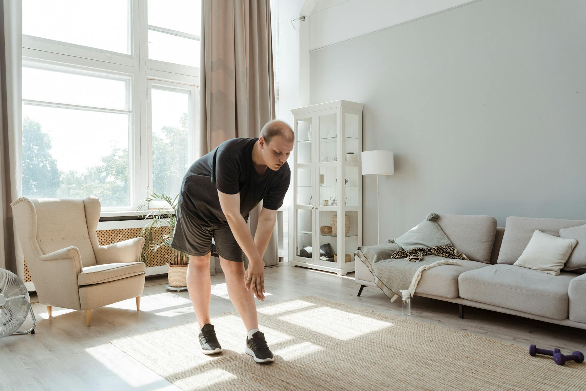 Person exercising and stretching in a living room with healthy food and a fitness tracker on a nearby table