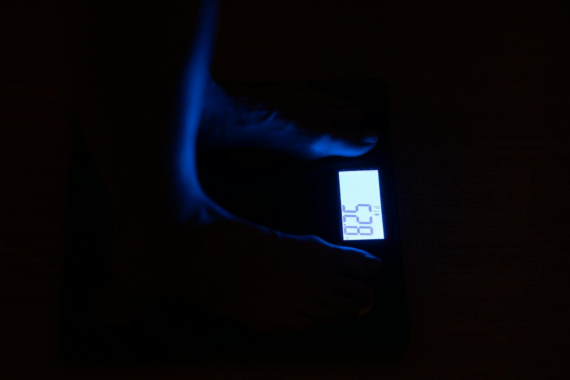 Person measuring body composition with skinfold calipers next to a kitchen scale and notebook with handwritten TDEE calculations