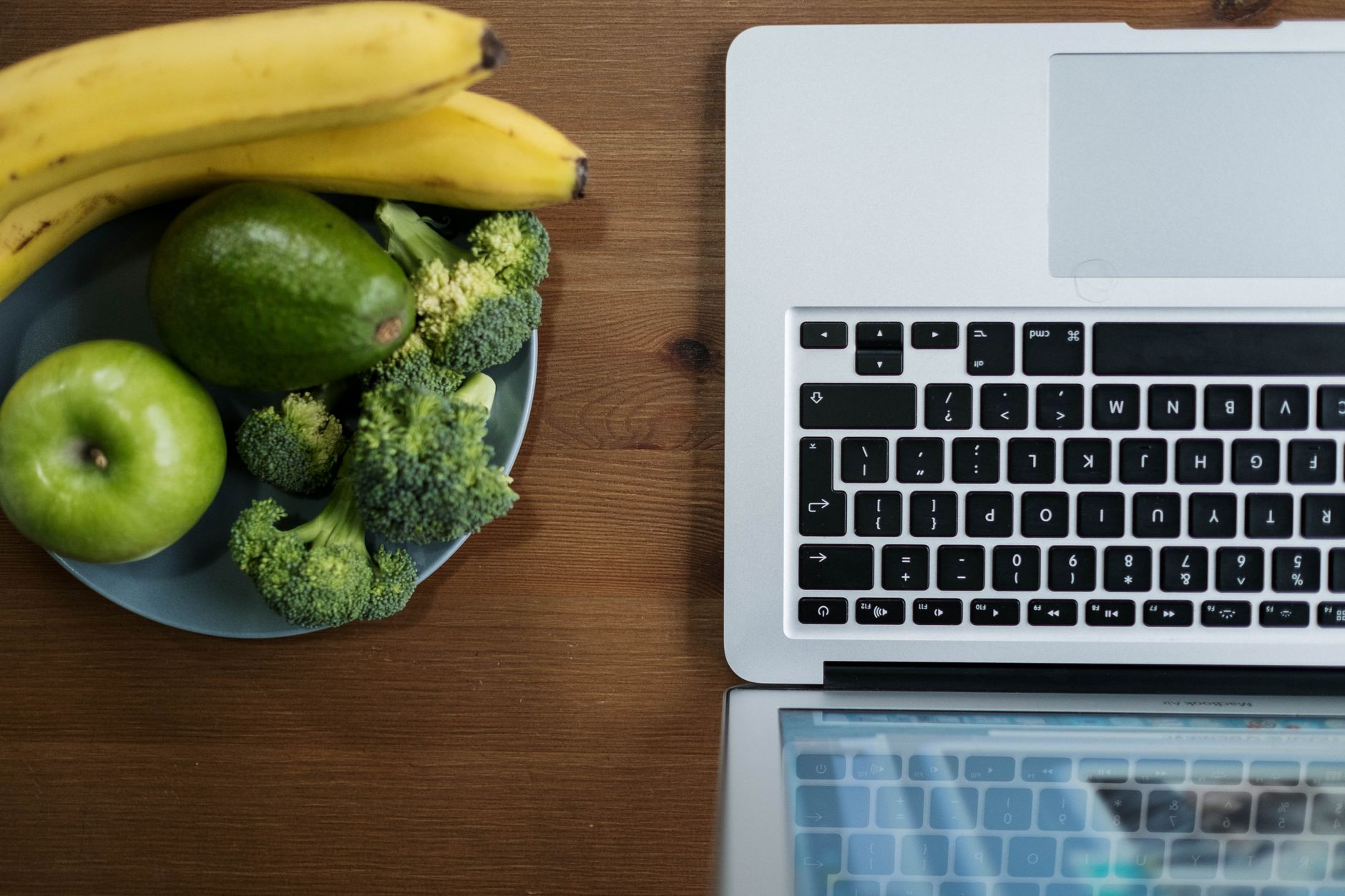 Open laptop showing the AFCD search interface beside fresh AU produce — bananas, an apple, a slice of wholemeal bread, and a small block of Vegemite — on a sunlit kitchen counter