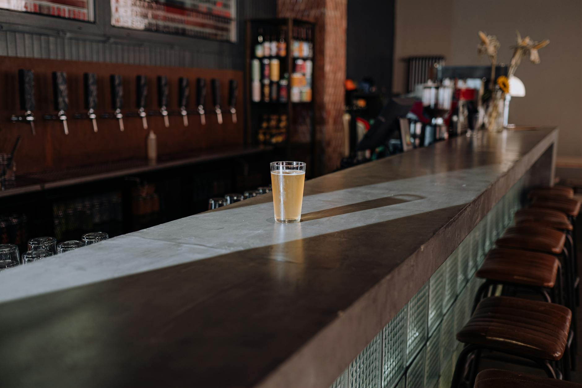 Four Australian beer glasses lined up on a wooden bar counter showing a pot, a schooner, a pint, and a small middy alongside a chalkboard with kilojoule values
