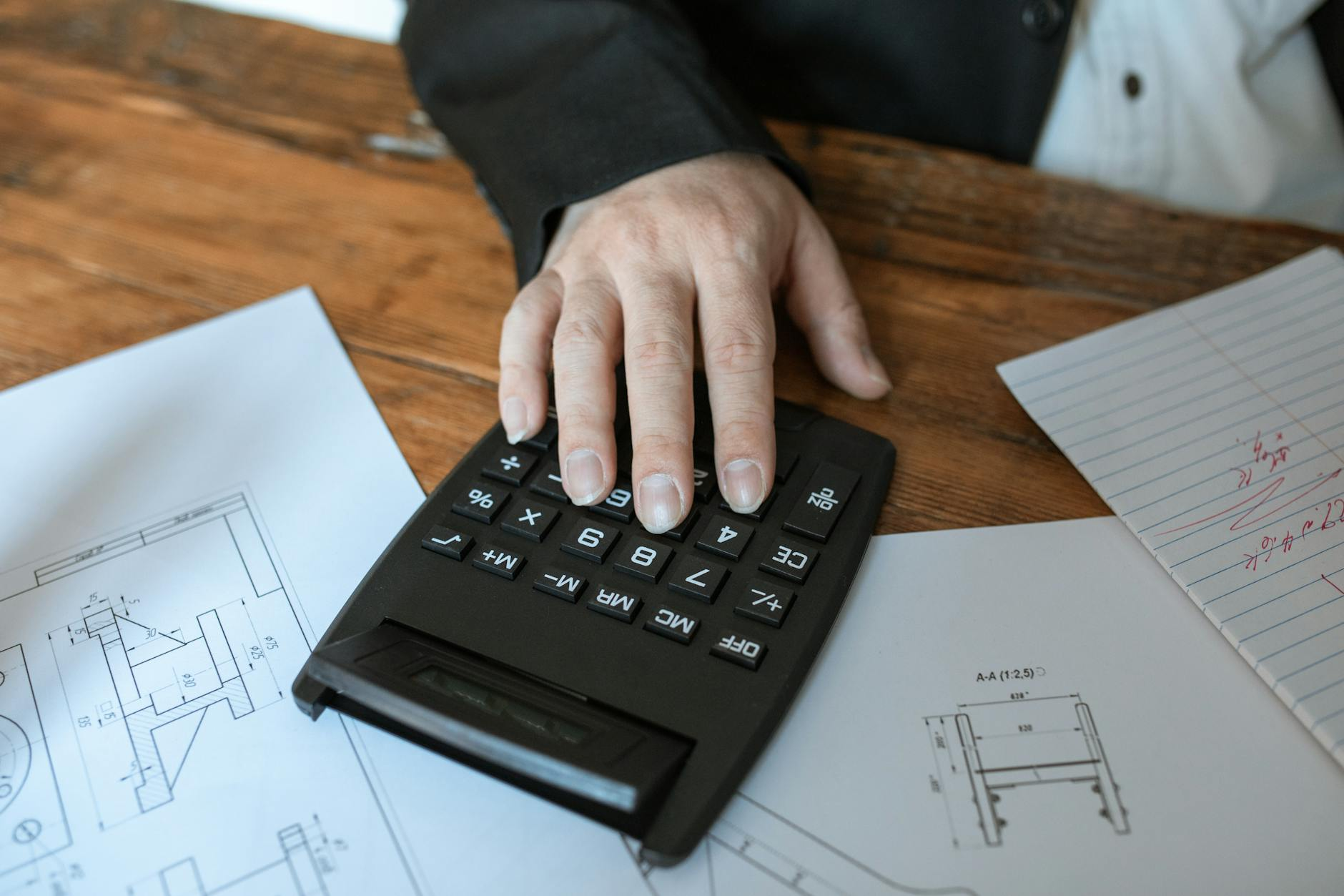 Notepad with handwritten Mifflin-St Jeor and Katch-McArdle TDEE calculations in kilojoules and kilocalories beside a calculator, measuring tape, and kitchen scale on a sunlit kitchen counter